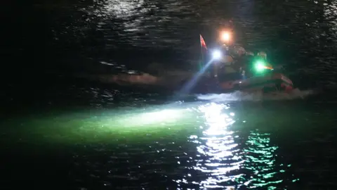 Eddie Mitchell A boat in the river. Spotlights are lighting up the water. 