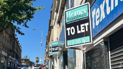 A series of empty shops with 'to let' signs above the windows