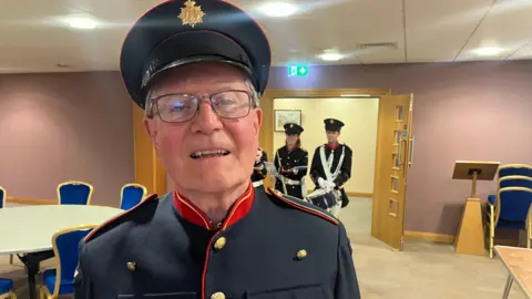 A man, wearing a navy uniform cap and jacket, looking at the camera. 