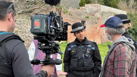 A film crew with actor Mandip Gill and other case members filming a scene. 