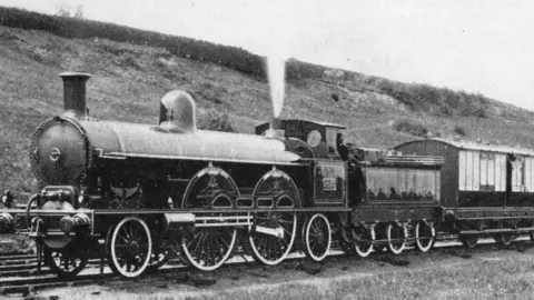 royaltrain.co.uk A black and white photo shows a steam locomotive pulling along the carts of the royal train.