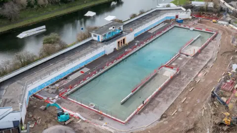 A blue swimming pool with a red and white border, which is next to a lake, 