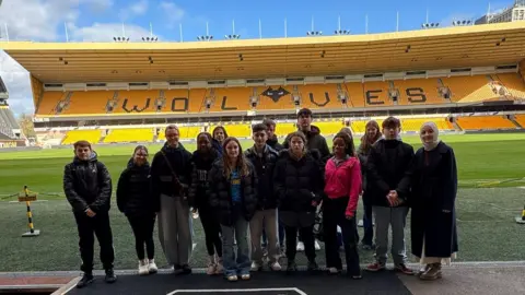 A group of teenagers in coats are stood together in the grounds of the Molineux Stadium