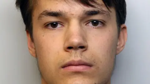 Mali Bennett-Smith, a teenage boy with dark brown hair and brown eyes, looking at the camera with no expression in a police mugshot.