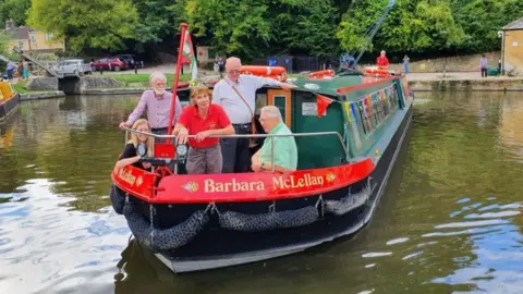 Kennet and Avon Canal Trust A canal boat, the Barbara McLellan, manoeuvres through a set of lock gates with five people in the stern.