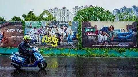 Getty Images A man drives past posters of regional films from India's Kerala-based Mollywood film industry, displayed along a street during protests against alleged sexual harassment allegations within the industry, in Kochi on August 30, 2024. 