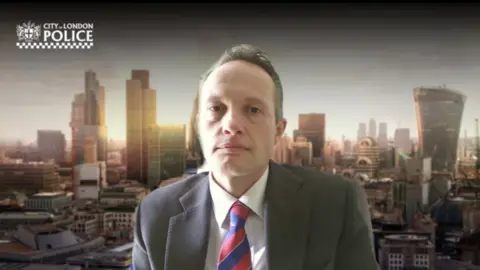 Det Supt Oliver Little on an online call looking at the camera, with a superimposed background of London's skyline.