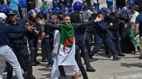 Getty Images An Algerian protester reacts during an anti-government demonstration outside La Grande Poste (main post office) in the centre of the capital Algiers on May 17, 2019. - Thousands of Algerians pushed through police tear gas and water cannon in the capital, to rally at the focal point of mass protests against the country's ruling elite. Riot police for hours prevented demonstrators from marching on the iconic central post office, with officials citing security concerns, but they ultimately gave way under pressure from the crowds.