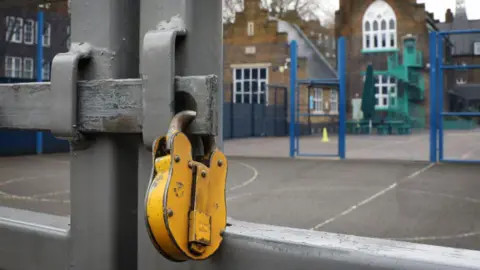Getty A yellow padlock on a school gate. The school can be seen in the background, on the other side of a playground.
