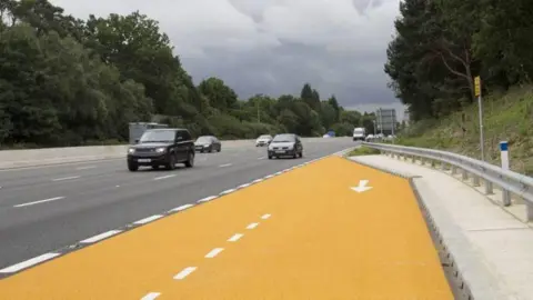 National Highways A view of an emergency area along the M1. The new area is yellow in colour and is sat at the side of the four-lane carriageway.