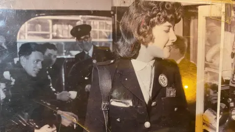 South Yorkshire Transport Museum A woman in bus conductor uniform stands inside a bus, with crew seated behind her drinking tea