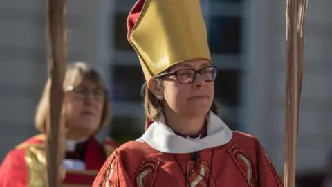 Bishop of Newcastle Helen-Ann Hartley wearing red robes and a yellow hat