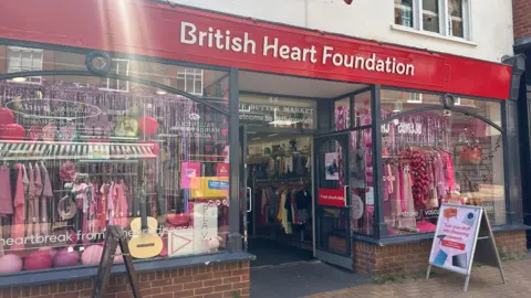 Alice Cunningham/BBC A British Heart Foundation with windows either side of its entrance filled with pink clothes, streamers and balloons.