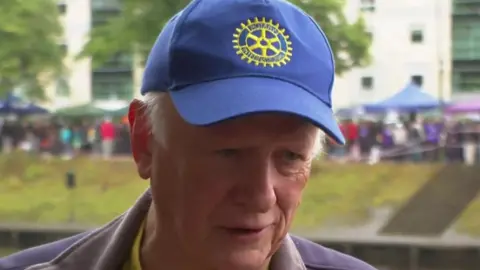 A head and shoulders view of Brian Joscelyne, who is wearing a blue cap with a yellow rotary club logo.