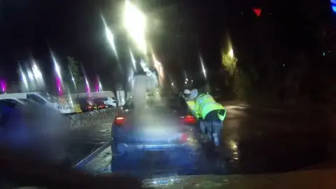 Dashcam image shows rear of car at night time with two police officers in hi-vis jackets leaning in to driver's door