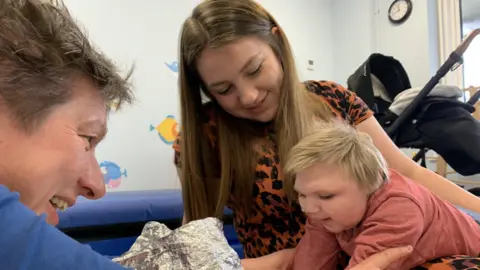 Toby Friedner/BBC Oakley playing with his mother and a charity worker