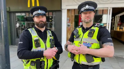 Two policeman stood in city centre high street in neon police vests