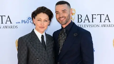Getty Images Emma and Matt Willis facing the camera, smiling. They are both wearing dark suits. Emma has cropped dark hair, and Matt has a shaved head.