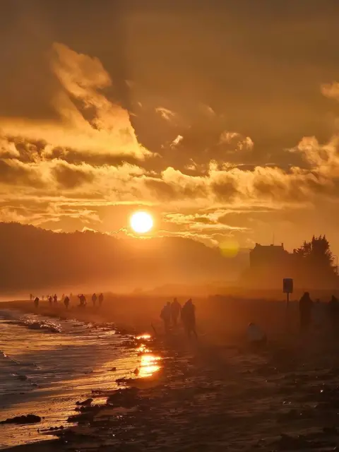 Scott Anderson An orange sunset sky over Broughty Ferry beach with people silhouetted along the shore.