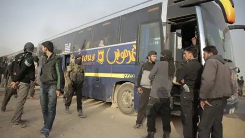 EPA Rebel fighters stand near government-supplied buses in the countryside of Damascus, Syria, on 26 March 2018