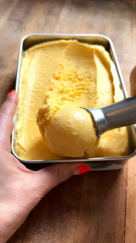 A tin of yellow sorbet with an ice cream scoop scooping up a ball of it.