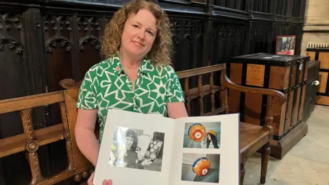 BBC/Joanita Musisi Laura is pictured sitting in the Minster holding up a scrapbook that contains childhood photos of her with her boss design