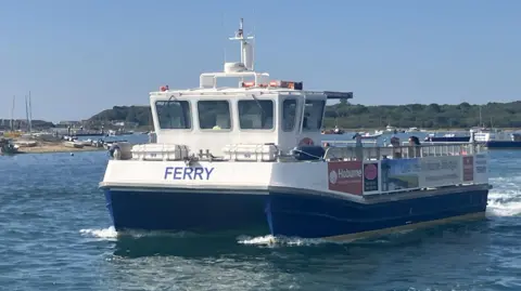 Supplied The Mudeford Ferry travels across Christchurch Harbour on a sunny day. The passenger vessel is viewed from the front with boats and the shoreline visible in the background.