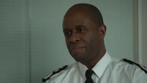 Deputy Assistant Commissioner Matt Ward, in police uniform, sits in an office infront of a window with a blind 