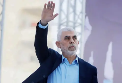 Getty Images Yahya Sinwar, wearing an open-necked shirt and smart jacket, raising his right hand in the air  