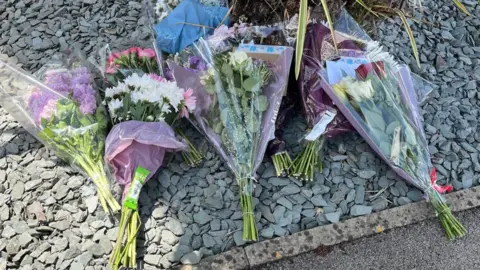 Ian Brown/BBC Several bouquets of flowers left on the front garden of a property.