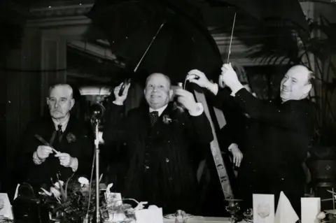 Getty Images Mr Albert Marchi, Chairman of the club addressing the diners at the luncheon under open umbrellas, while fellow member sprinkles him with salt. Another member on the left has two knives crossed, London, England. (Photo by Hulton Archive/Getty Images) DEFYING FATE.
-Members of the "13 Club" are shown at
luncheon on February 13 at the Cafe Royal in London The chairman
(Mr Albert Minchin), who has just recovered from two broken legs, is
shown being christened with salt as he stands beneath an umbrella which
he has just opened indoors