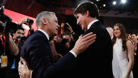 Reuters Mark Carney y Justin Trudeau se abrazan cuando una multitud de fotógrafos toman fotos y la hija de Trudeau, que había presentado a su padre en el evento del Partido Liberal, mira. 