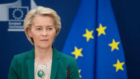 European Commission President Ursula von der Leyen sitting in front of the EU flag