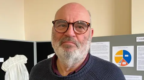 Tom Jackson/BBC Andrew Spooner looking at the camera, behind him are some museum exhibits unrelated to the bone.