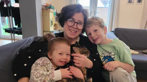 Jonny Coxon Charlotte wearing a black top cuddling with Thomas in a green Sonic t-shirt and Anna in a floral jumper and a cat