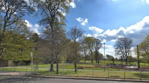 Google Seven Oaks Park in Cramlington, showing a patch of grass, trees not yet in leaf and children's playground equipment