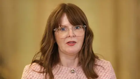PA Media Caoimhe Archibald, with long brown hair, wearing glasses and a pink jacket. 