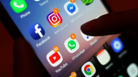 A finger hovering over a series of Apps on a mobile phone, including Facebook and WhatsApp.