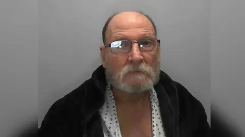 An older man wearing glasses and a dressing gown over a pajama top