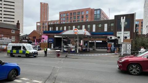 BBC A police van and officer next to a police cordon, with blue and white police tape blocking the entrance of 