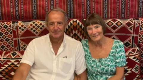 Stuart Wilson A man and a woman sat together on a sofa looking towards the camera.