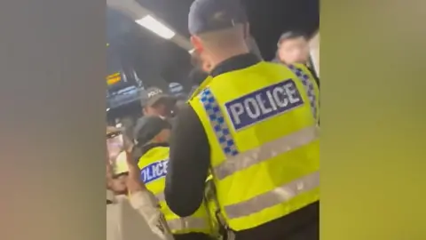 Dave Skerton Police officers from behind with hi-vis vests on putting people on to trains at Manchester Victoria railway station