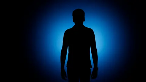 Thomas Trutschel Silhouette of a man standing in front of a blue background.