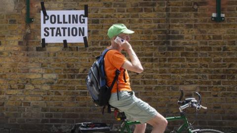 Man on a bike speaking into a mobile phone outside a polling station