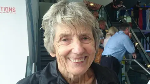 Paul Burnell/BBC Sue Lopez has grey hair and a black shirt -she stands in the foyer of the National Football Museum