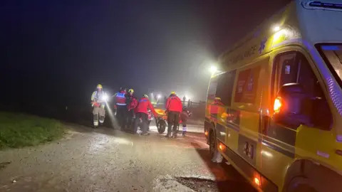 Wiltshire Search and Rescue A team of rescuers move a stretcher over a path next to a yellow ambulance