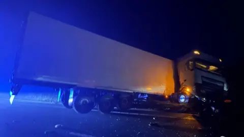 White HGV crashed at the side of a road at night.