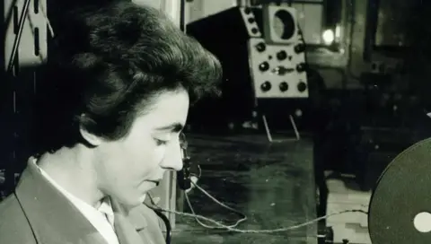 Dame Stephanie Shirley Dame Stephanie está pintada en una fotografía en blanco y negro y con una camisa y una chaqueta con dispositivos técnicos en el fondo