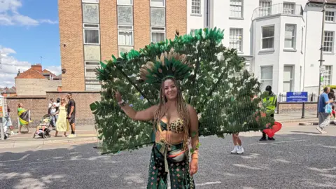 A woman standing in a street dressed in green with groups of people in the background