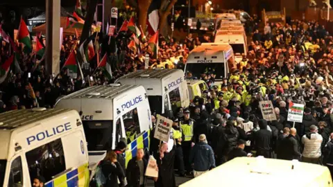 Getty Images A long line of police vans, with people on both sides. Some are police officers, others hold placards and flags